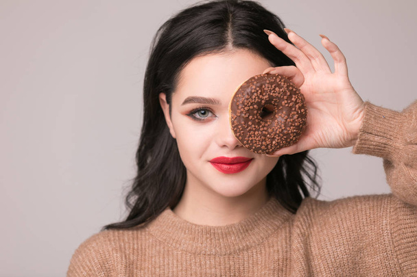 beautiful girl with red lips posing with donuts.Pretty sexy brunette girl with long hair, glossy red lips, holding tasty donut with hand, looking at camera. Dark gray background, copy space - Foto, Imagem