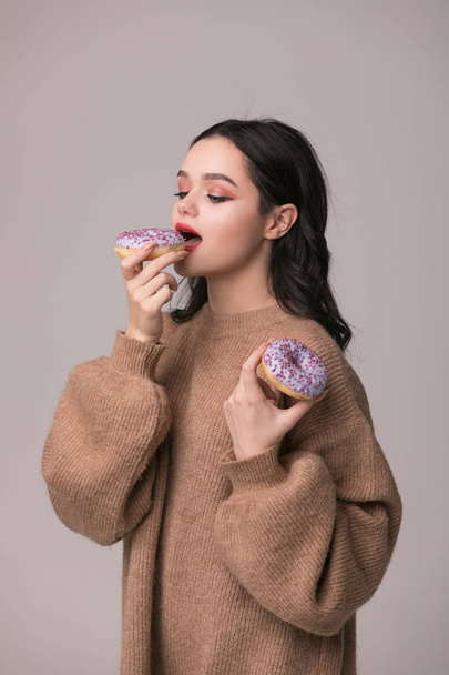 beautiful girl with red lips posing with donuts.Pretty sexy brunette girl with long hair, glossy red lips, holding tasty donut with hand, looking at camera. Dark gray background, copy space - Photo, Image