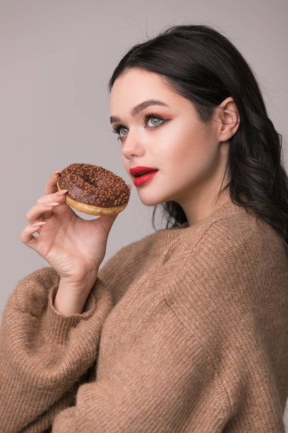 beautiful girl with red lips posing with donuts.Pretty sexy brunette girl with long hair, glossy red lips, holding tasty donut with hand, looking at camera. Dark gray background, copy space - Foto, Imagen