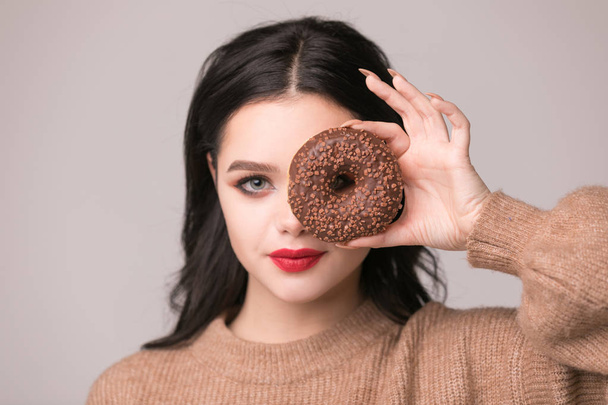beautiful girl with red lips posing with donuts.Pretty sexy brunette girl with long hair, glossy red lips, holding tasty donut with hand, looking at camera. Dark gray background, copy space - Photo, image