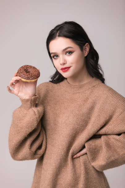 beautiful girl with red lips posing with donuts.Pretty sexy brunette girl with long hair, glossy red lips, holding tasty donut with hand, looking at camera. Dark gray background, copy space - Foto, afbeelding