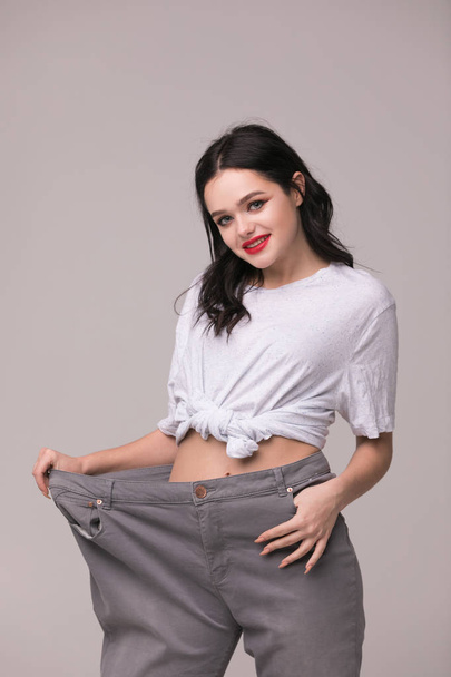 Weight loss concept - slim woman is happy to show her big old trousers.Thin woman in big pants - weight loss concepts - Photo, Image