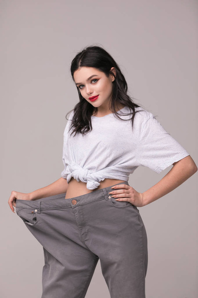 Weight loss concept - slim woman is happy to show her big old trousers.Thin woman in big pants - weight loss concepts - Photo, image