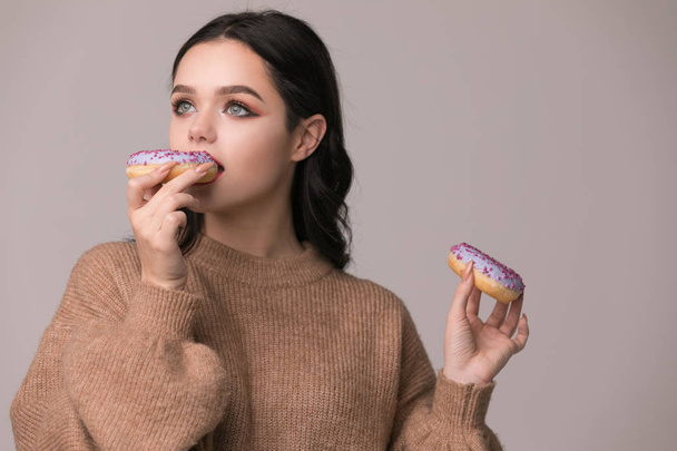 beautiful girl with red lips posing with donuts and apple.Pretty sexy brunette girl with long hair, glossy red lips, holding tasty donut with hand, looking at camera. - Foto, afbeelding