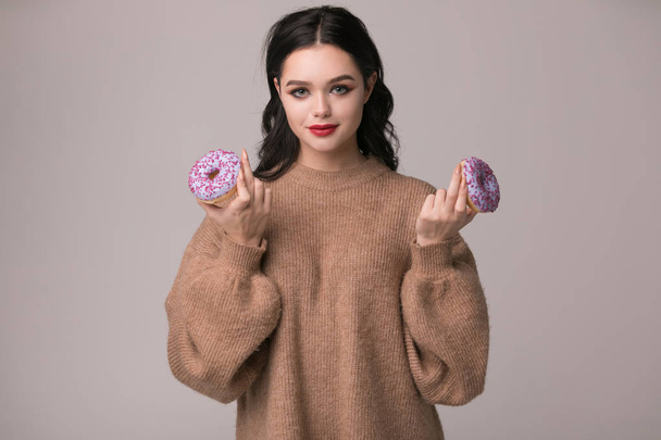 beautiful girl with red lips posing with donuts and apple.Pretty sexy brunette girl with long hair, glossy red lips, holding tasty donut with hand, looking at camera. - Fotoğraf, Görsel