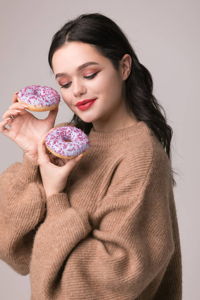 beautiful girl with red lips posing with donuts and apple.Pretty sexy brunette girl with long hair, glossy red lips, holding tasty donut with hand, looking at camera. - Φωτογραφία, εικόνα