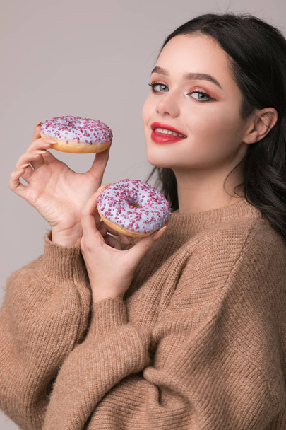 beautiful girl with red lips posing with donuts and apple.Pretty sexy brunette girl with long hair, glossy red lips, holding tasty donut with hand, looking at camera. - Foto, Imagem