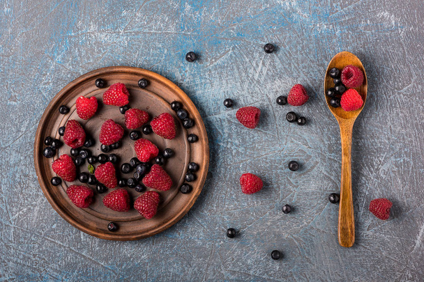 Blueberries and raspberries in an old-fashioned container on a gray concrete background - Photo, image