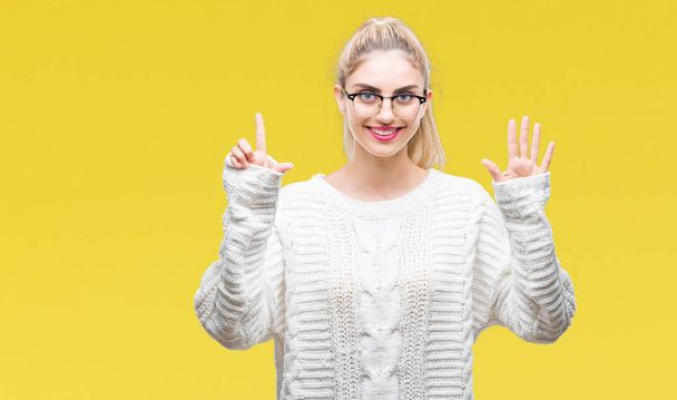 Young beautiful blonde woman wearing glasses over isolated background showing and pointing up with fingers number seven while smiling confident and happy. - Photo, Image