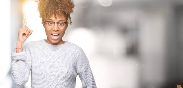Красивая молодая африканская американка в зимнем свитере на изолированном фоне показывает пальцем на успешную идею. Взволнован и счастлив. Номер один
. - Фото, изображение
