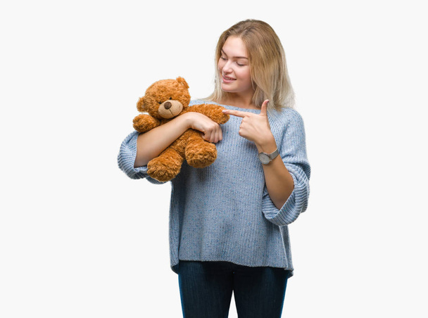 Young caucasian woman holding cute teddy bear over isolated background very happy pointing with hand and finger - Foto, Imagen