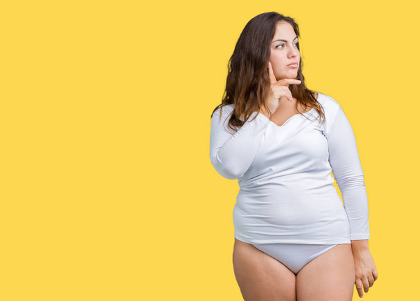 Beautiful plus size young overwight woman wearing white underwear over isolated background with hand on chin thinking about question, pensive expression. Smiling with thoughtful face. Doubt concept. - Photo, image