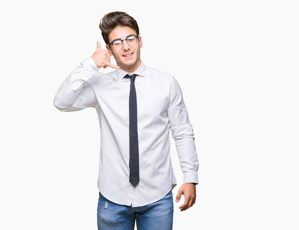 Молодой бизнесмен в очках на изолированном фоне улыбается, делая телефонный жест рукой и пальцами, как будто разговаривая по телефону. Коммуникационные концепции
. - Фото, изображение