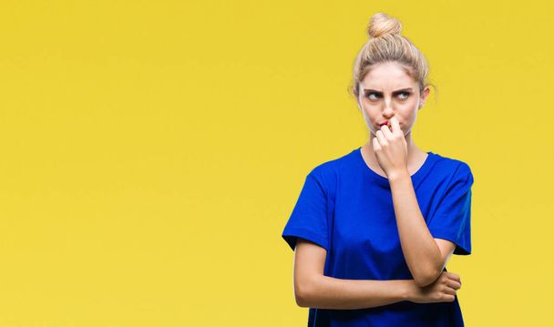 Jonge mooie blond en blauwe ogen vrouw blauw t-shirt dragen over geïsoleerde achtergrond op zoek gestresst en nerveus met handen op mond nagels te bijten. Angst probleem. - Foto, afbeelding