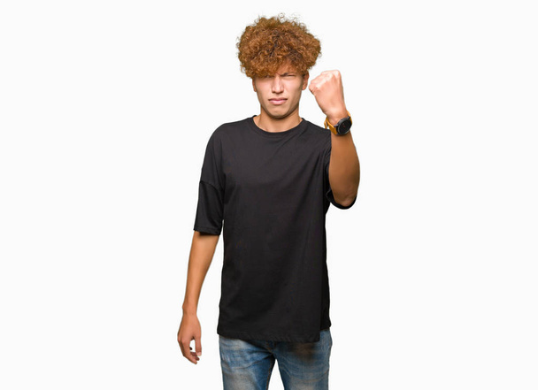 Jonge knappe man met afro haar dragen zwart t-shirt boos en gekke verhogen vuist gefrustreerd en woedend terwijl schreeuwen met woede. Woede en agressief concept. - Foto, afbeelding