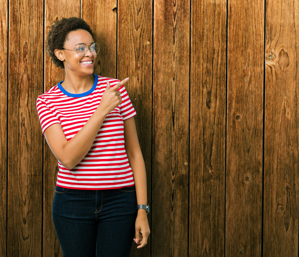 Kaunis nuori afrikkalainen amerikkalainen nainen yllään lasit yli eristetty tausta iloinen hymy kasvojen osoittaa käsi ja sormi jopa puolelle onnellinen ja luonnollinen ilme kasvoilla
 - Valokuva, kuva
