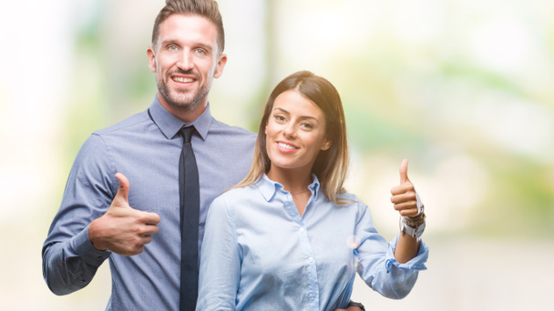Young workers business couple over isolated background doing happy thumbs up gesture with hand. Approving expression looking at the camera with showing success. - Photo, image