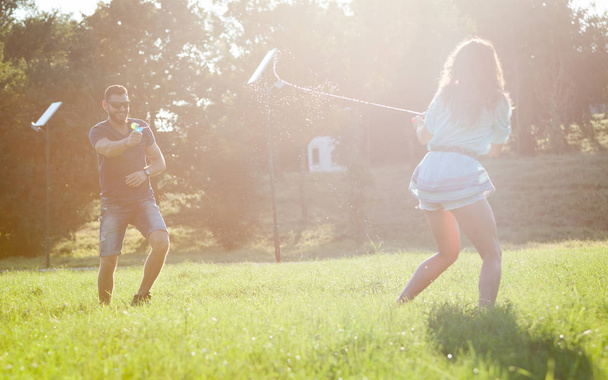 Игривая молодая пара, гоняющаяся друг за другом и играющая с водяными пистолетами на лугу на закате
. - Фото, изображение