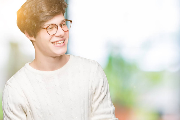 Young handsome man wearing glasses over isolated background looking away to side with smile on face, natural expression. Laughing confident. - Photo, image
