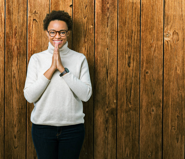 Jeune belle femme afro-américaine portant des lunettes sur fond isolé priant avec les mains ensemble demandant pardon souriant confiant
. - Photo, image