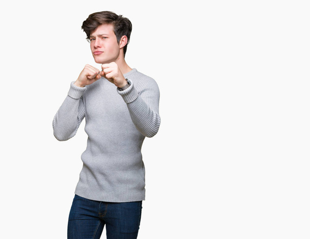 Joven hombre guapo vistiendo suéter de invierno sobre fondo aislado Listo para luchar con el gesto de defensa del puño, cara enojada y molesta, miedo al problema
 - Foto, Imagen