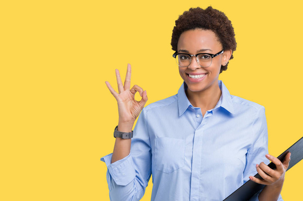 優秀なシンボルの指で ok サインをして孤立した背景にクリップボードを保持している若いアフリカ系アメリカ人ビジネス女性 - 写真・画像