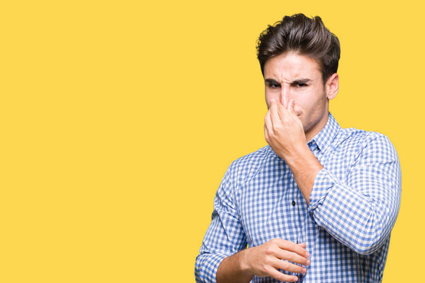 Young handsome business man over isolated background smelling something stinky and disgusting, intolerable smell, holding breath with fingers on nose. Bad smells concept. - Photo, Image