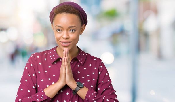 Linda jovem afro-americana vestindo lenço na cabeça sobre fundo isolado orando com as mãos juntas pedindo perdão sorrindo confiante
. - Foto, Imagem