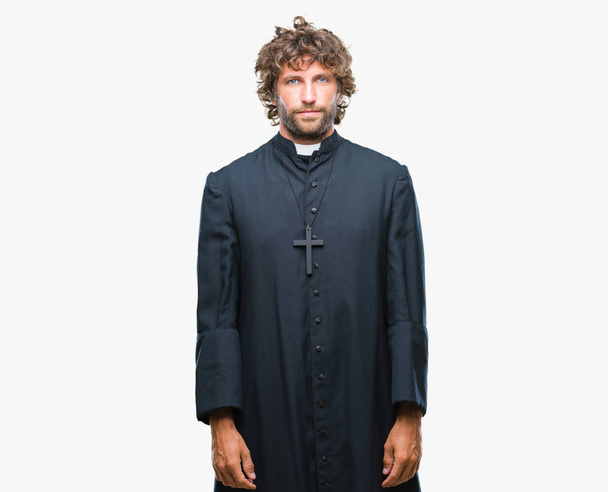 Handsome hispanic catholic priest man over isolated background with serious expression on face. Simple and natural looking at the camera. - Фото, зображення