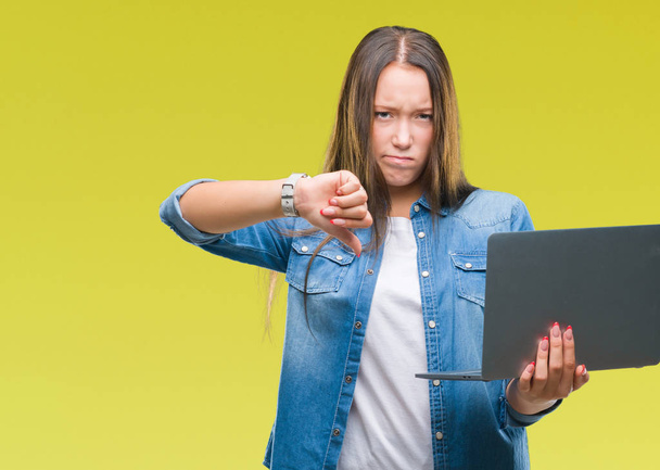 Young caucasian woman using laptop over isolated background with angry face, negative sign showing dislike with thumbs down, rejection concept - Valokuva, kuva