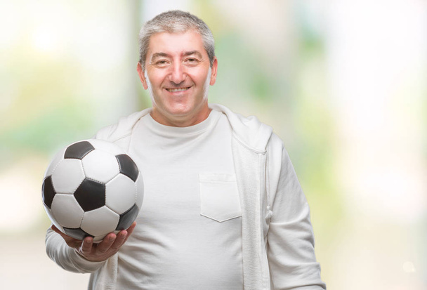 Красивый пожилой человек держит футбольный мяч на изолированном фоне со счастливым лицом стоя и улыбаясь с уверенной улыбкой показывая зубы
 - Фото, изображение