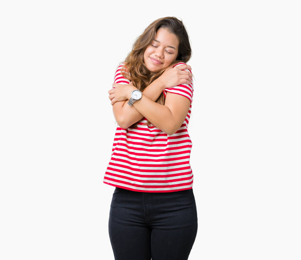 Jonge mooie brunette vrouw dragen strepen t-shirt over geïsoleerde achtergrond knuffelen zich gelukkig en positief, zeker glimlachen. Eigenliefde en zelfzorg - Foto, afbeelding