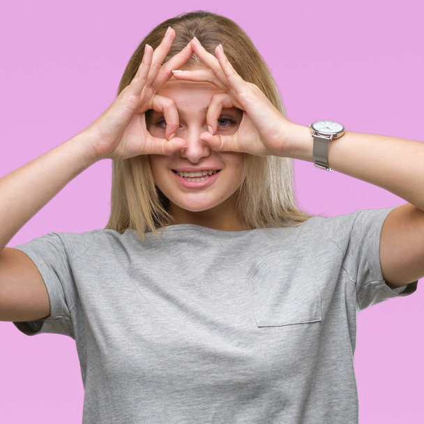 Young caucasian woman over isolated background doing ok gesture like binoculars sticking tongue out, eyes looking through fingers. Crazy expression. - Fotoğraf, Görsel