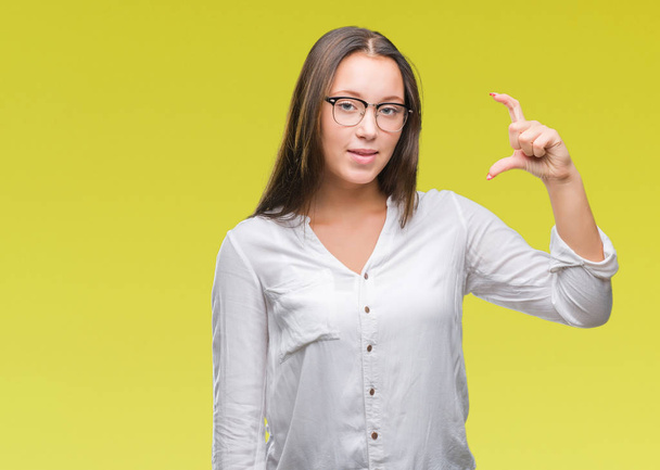 Young caucasian beautiful business woman wearing glasses over isolated background smiling and confident gesturing with hand doing size sign with fingers while looking and the camera. Measure concept. - Photo, Image