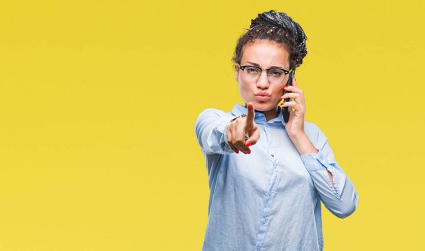 Young braided hair african american business girl showing calling using smartphone over isolated background pointing with finger to the camera and to you, hand sign, positive and confident gesture from the front - 写真・画像