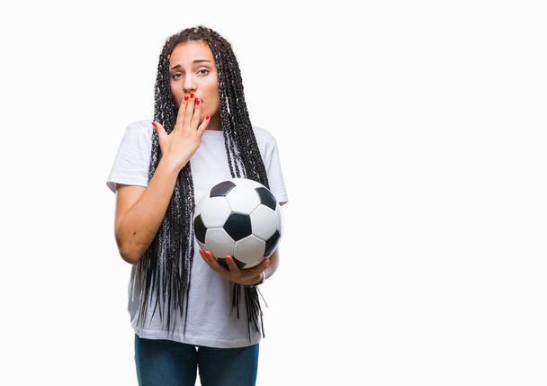 Joven chica afroamericana trenzada pelo sosteniendo pelota de fútbol sobre fondo aislado cubrir la boca con la mano conmocionado con vergüenza por error, expresión de miedo, asustado en silencio, concepto secreto
 - Foto, imagen