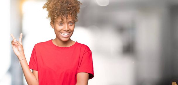schöne junge afrikanisch-amerikanische Frau über isoliertem Hintergrund lächelnd mit glücklichem Gesicht, das in die Kamera zwinkert und Siegeszeichen macht. Nummer zwei. - Foto, Bild
