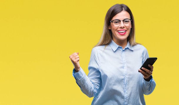 Young beautiful business woman texting message using smartphone over isolated background screaming proud and celebrating victory and success very excited, cheering emotion - Photo, image