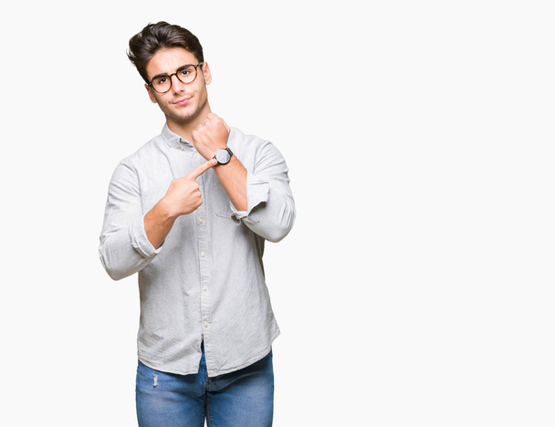 Young handsome man wearing glasses over isolated background In hurry pointing to watch time, impatience, upset and angry for deadline delay - Foto, Imagem