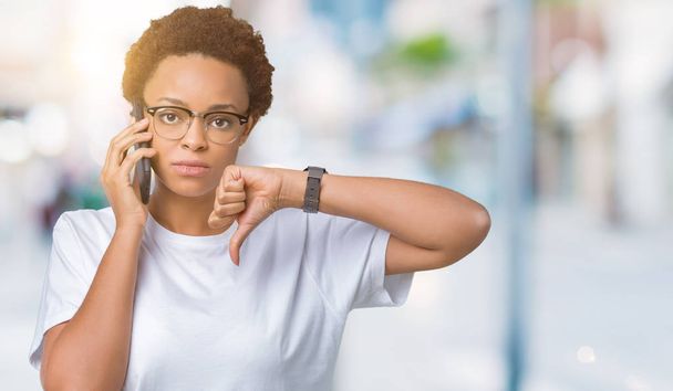 Fiatal afrikai-amerikai nő beszél a telefonon felett Haragos arc, negatív előjellel mutatja ellenszenv a hüvelykujját lefelé, elutasítás koncepció elszigetelt háttér - Fotó, kép