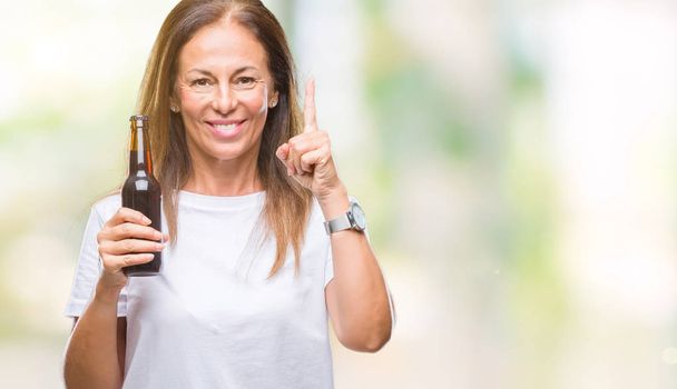 Mujer hispana de mediana edad bebiendo cerveza sobre un fondo aislado sorprendida con una idea o pregunta apuntando con el dedo con cara feliz, número uno
 - Foto, imagen