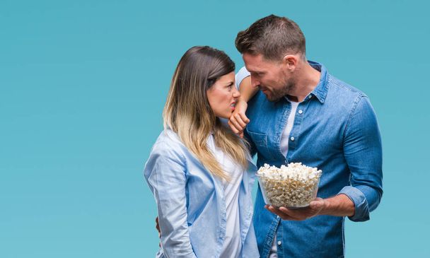 Young couple in love eating popcorn over isolated background annoyed and frustrated shouting with anger, crazy and yelling with raised hand, anger concept - Zdjęcie, obraz