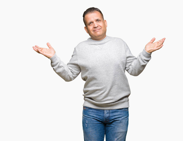 Średnim wieku Emiraty człowiek noszenie bluzy sportowe nad wyrażenie clueless i mylić na białym tle z ramiona i ręce podniesione. Koncepcja wątpliwości. - Zdjęcie, obraz