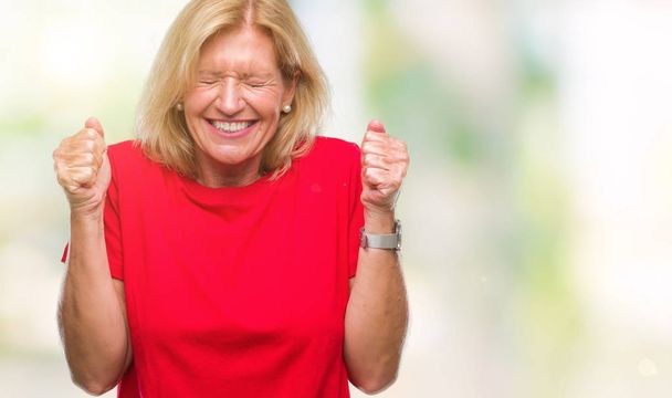 Mujer rubia de mediana edad sobre un fondo aislado emocionada por el éxito con los brazos levantados celebrando la victoria sonriendo. Concepto ganador
. - Foto, Imagen