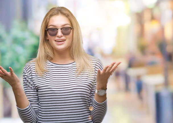 Jeune femme caucasienne portant des lunettes de soleil sur fond isolé célébrant fou et étonné pour le succès avec les bras levés et les yeux ouverts hurlant excités. Concept gagnant
 - Photo, image