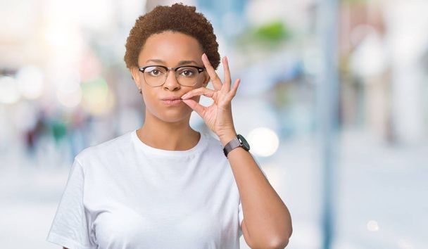 Krásná mladá africká americká žena nosí brýle nad izolované pozadí ústa a rty jako zip s prsty. Tajné a tiché, tabu mluví - Fotografie, Obrázek