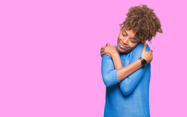 Mooie jonge Afro-Amerikaanse vrouw op geïsoleerde achtergrond knuffelen zich gelukkig en positief, zeker glimlachen. Eigenliefde en zelfzorg - Foto, afbeelding