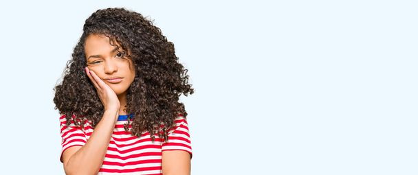 Young beautiful woman with curly hair wearing stripes t-shirt thinking looking tired and bored with depression problems with crossed arms. - Photo, Image