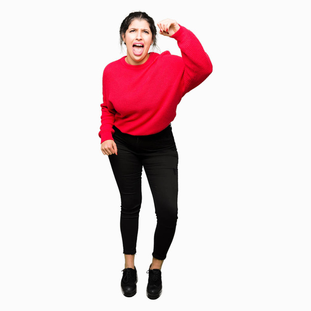 Jovem mulher bonita vestindo camisola vermelha e pão irritado e louco levantando punho frustrado e furioso enquanto gritando com raiva. Raiva e conceito agressivo
. - Foto, Imagem