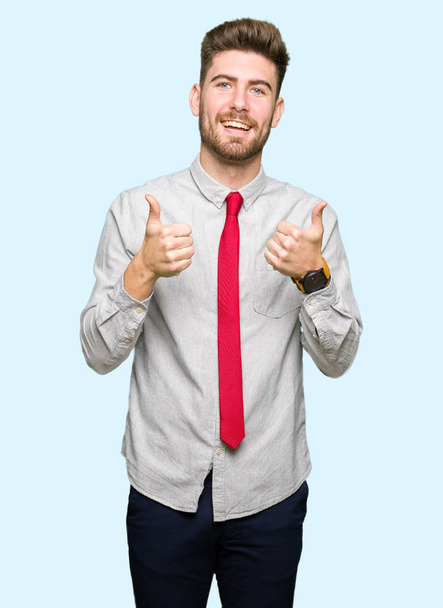 Young handsome business man success sign doing positive gesture with hand, thumbs up smiling and happy. Looking at the camera with cheerful expression, winner gesture. - Фото, изображение